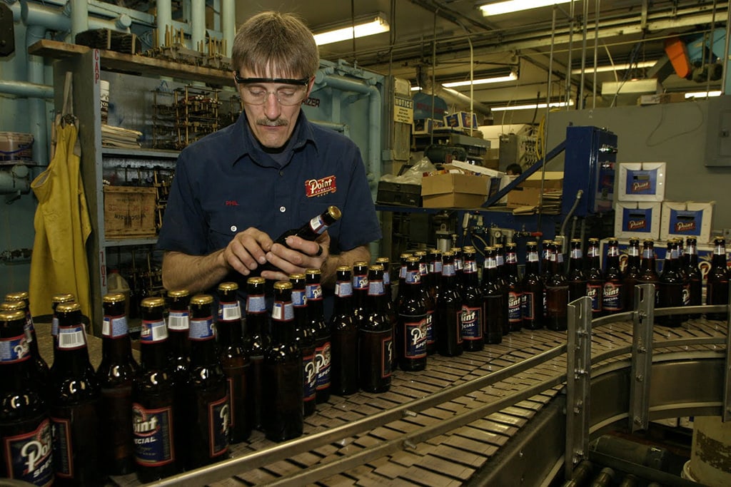 A man working on the bottling line inspects a bottle of Point Special beer